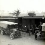 greyscale photo of vehicles beside train