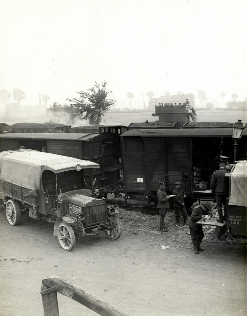 greyscale photo of vehicles beside train